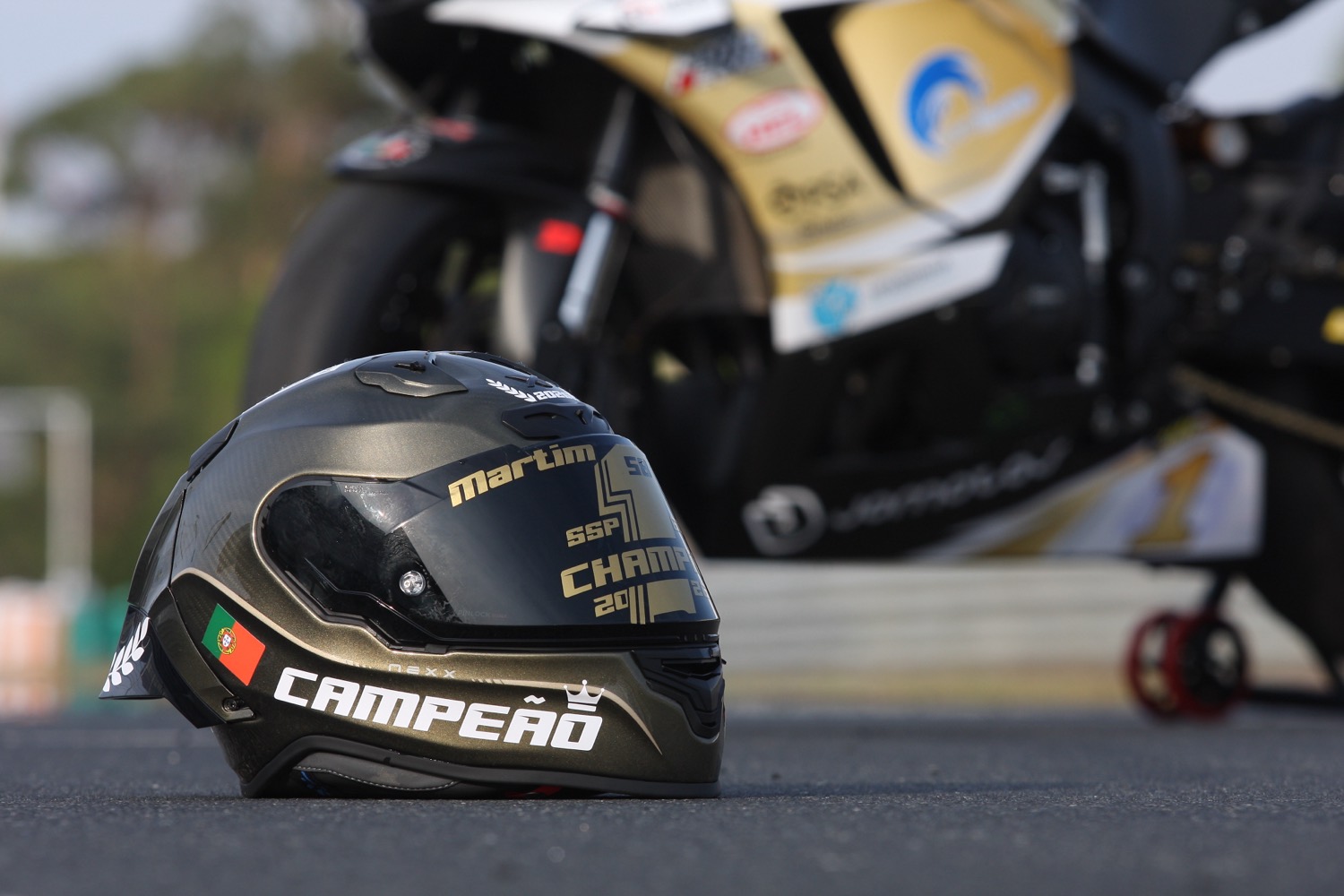 Capacete CAMPEÃO pousado no asfalto à frente da mota dourada