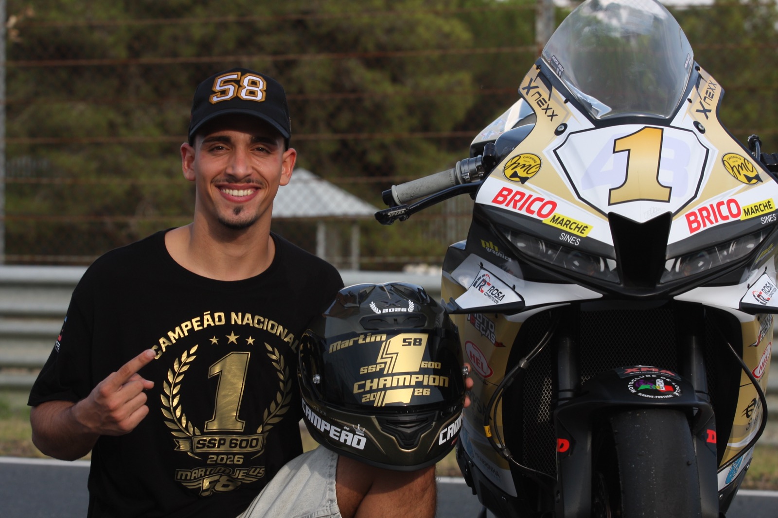 Martim de t-shirt de Campeão Nacional SSP 600 2026, com o capacete CAMPEÃO, ao lado da mota dourada com o número 1